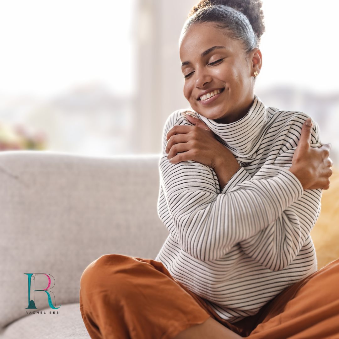 Lady smiling and hugging herself whilst sitting cross legged taking care of her wellbeing