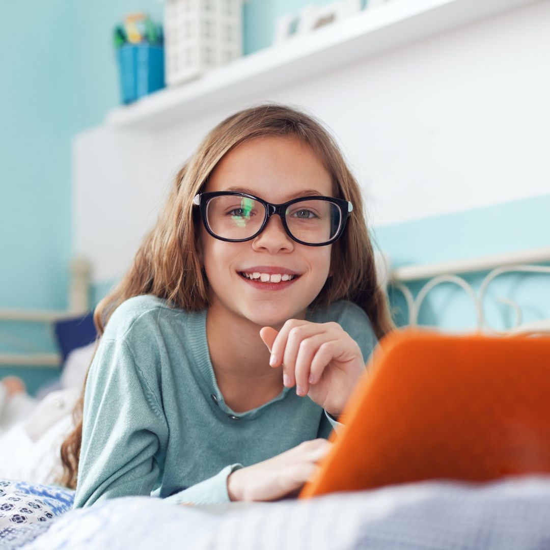 Child of 8 years old smiling at the camera. She is wearing glasses and looking studios